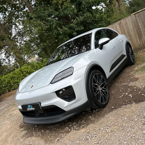 White Porsche SUV parked on gravel near wooden fence.