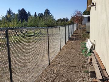 Long chain-link fence alongside a building on a sunny day.