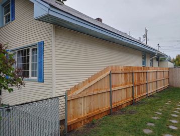 A beige house with blue window shutters and a new wooden fence in the yard.