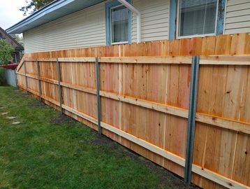 Freshly installed wooden fence with metal supports along a house.