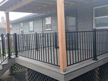 Covered porch with black railing and wooden posts attached to a house.