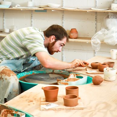 A man shapes clay pottery on a potter's wheel in a workshop.