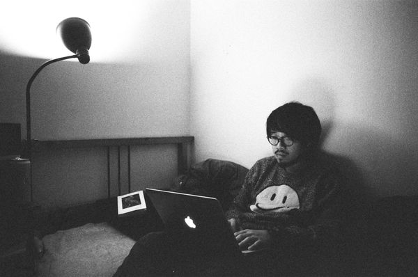 Lawrence Lai sitting on a bed, using computer.