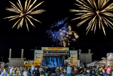 Fireworks light up the night sky over a concert stage with an audience.