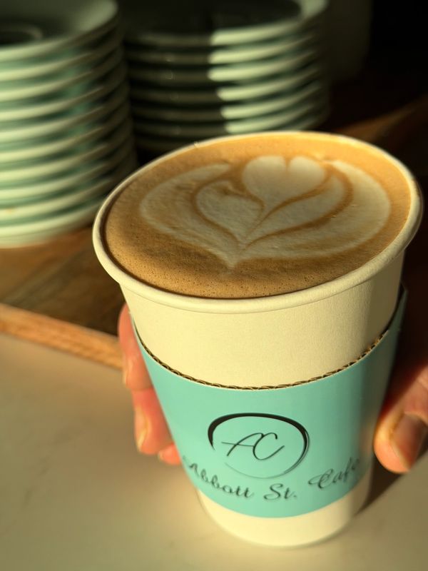 A latte with heart-shaped latte art in a cup with a blue sleeve.