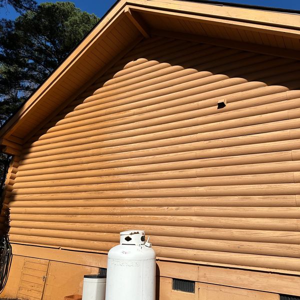 A large propane tank outside a wooden cabin under clear blue sky.