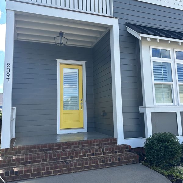 Gray house exterior with a bright yellow front door and brick steps.
