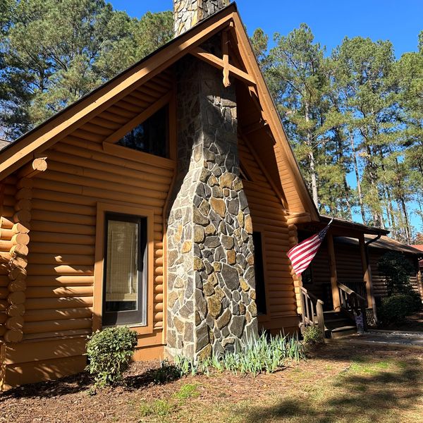 Cozy log cabin with stone chimney and American flag under clear blue sky.