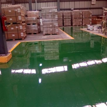 A shiny green epoxy floor in a warehouse with stacked boxes.
