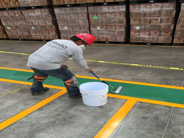 Worker painting green lines in a warehouse with safety gear.