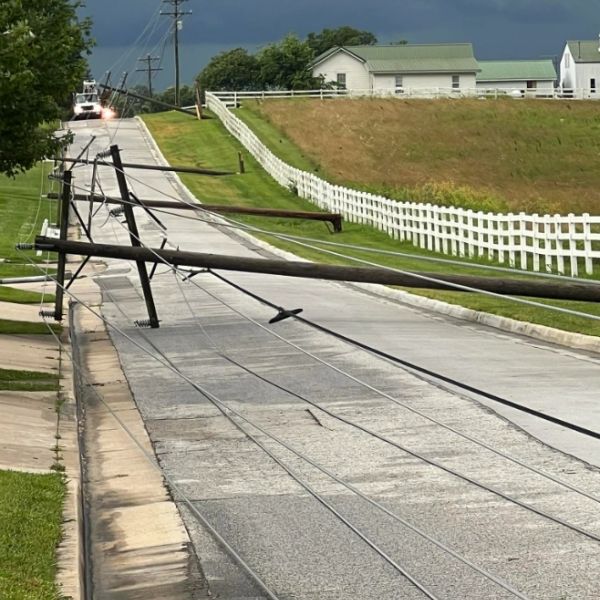 Downed power poles blocking a road in a rural area.