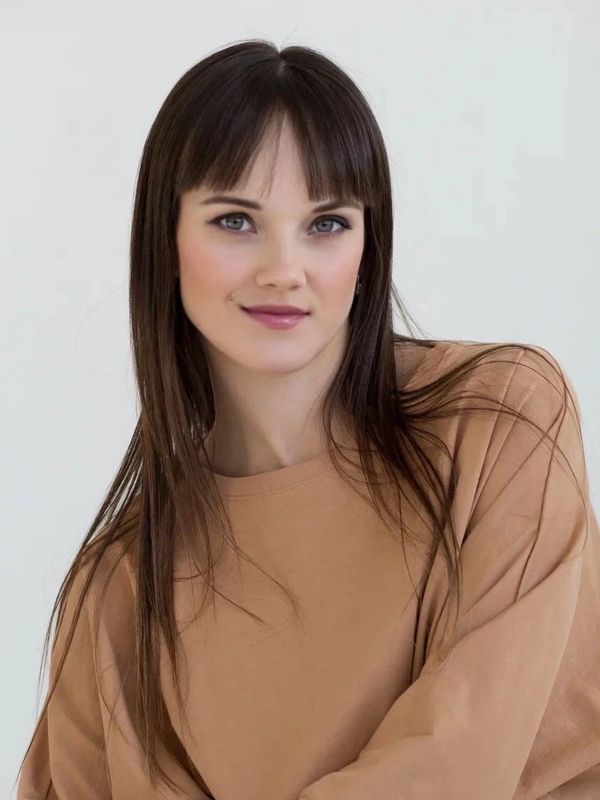 Young woman with straight brown hair and beige sweater.