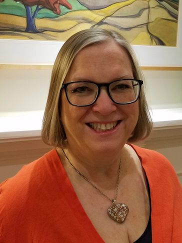 Smiling woman with glasses and heart-shaped necklace.