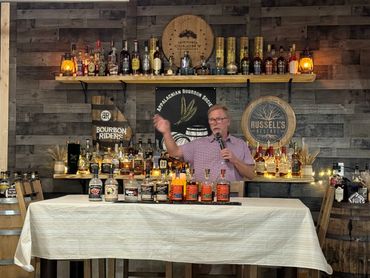 A man presents various whiskey bottles at a tasting event.