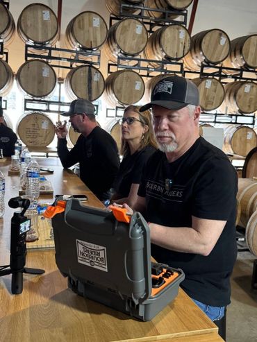 People tasting drinks in a distillery with barrels in the background.