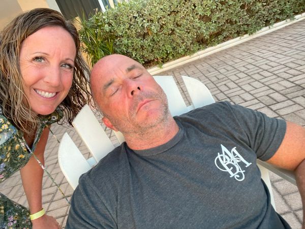 Woman smiling next to a sleeping man on a chair outdoors.
