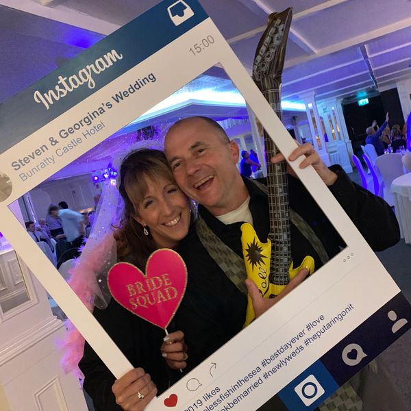 Couple joyfully posing with Instagram frame at a wedding celebration.