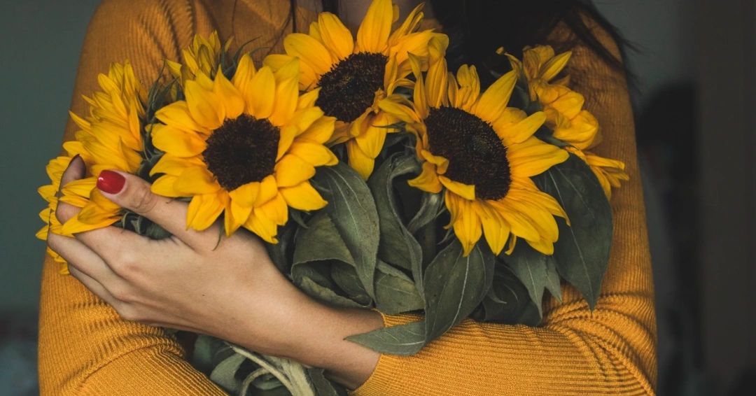 Person in a yellow sweater holding a bouquet of sunflowers, symbolizing warmth and support.