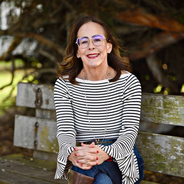Woman in striped top sitting on a wooden bench outdoors, smiling warmly.