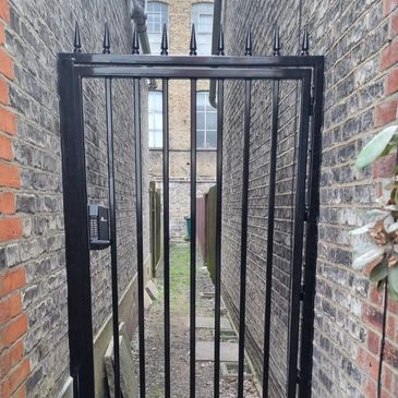 A black metal gate blocking a narrow alley between brick buildings.