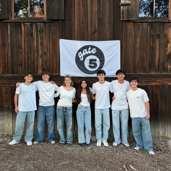 Group of seven people posing in front of a wooden wall with a Gate 5 sign.