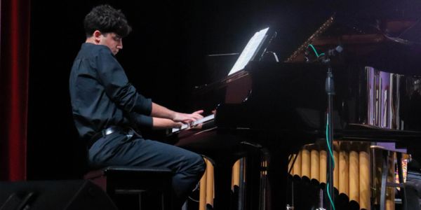 Young man playing grand piano on stage.