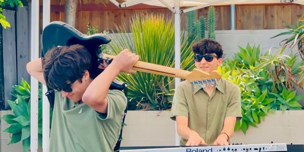 Two young men playing instruments outside in greenery.