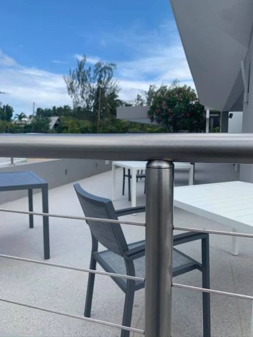 Modern outdoor patio with metal railing and chairs under a blue sky.