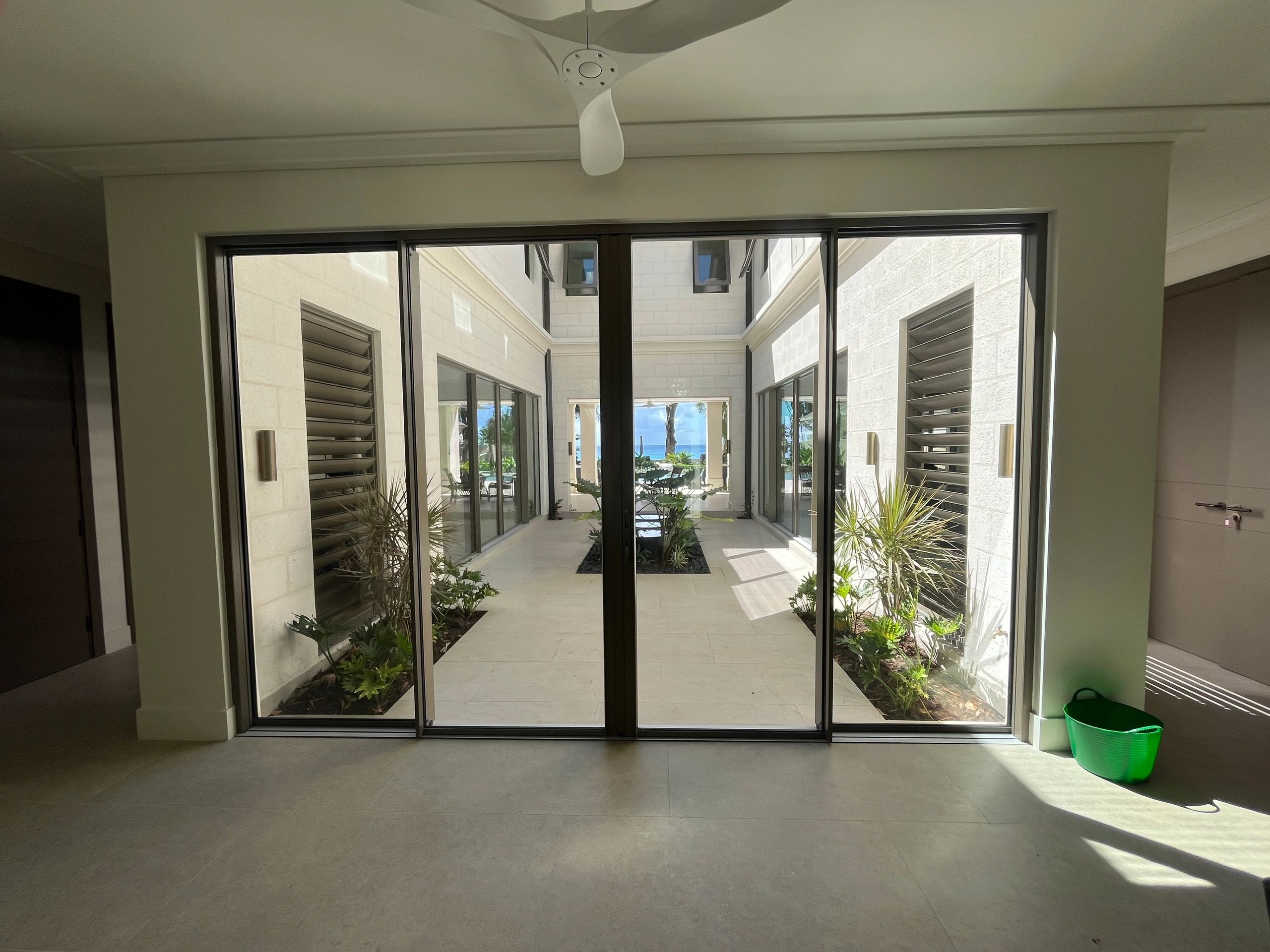 View through glass doors to a bright courtyard with plants and ocean in the distance.