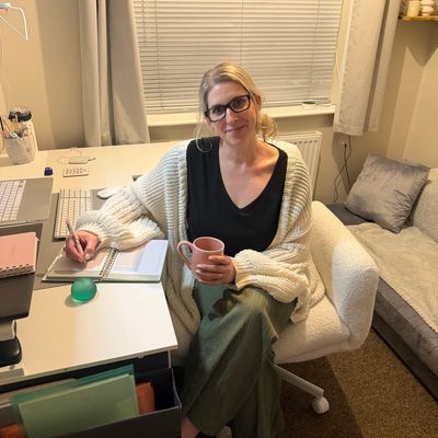 Woman sitting at desk, writing and holding a mug.