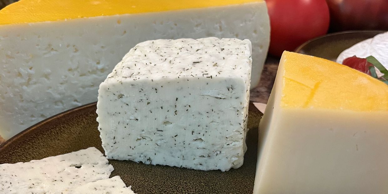 Variety of cheeses including herb-infused and wax-coated blocks on a plate.