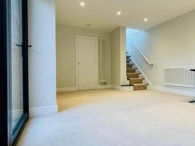 Empty modern room with beige carpet and staircase leading upstairs.