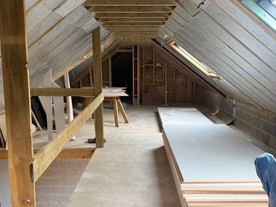 An unfinished attic space under construction with drywall sheets stacked.