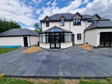 Modern white two-story house with a glass conservatory and paved driveway.