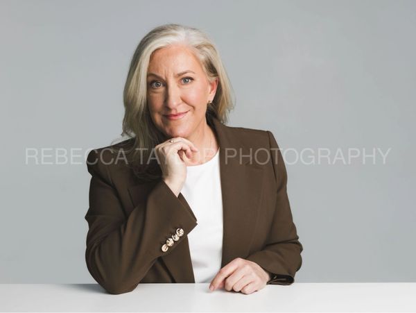 Professional woman with gray hair in a brown blazer smiling confidently.