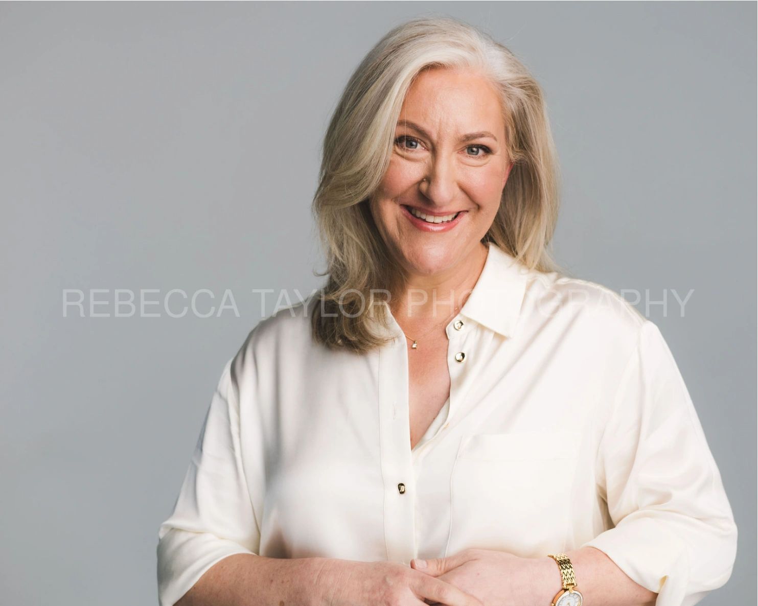 Smiling mature woman in white shirt against grey background.