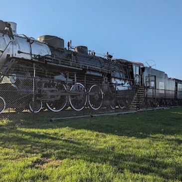 A vintage steam locomotive displayed outdoors behind a fence.