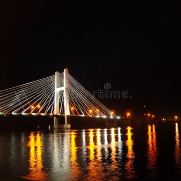 Cable-stayed bridge illuminated at night with reflections on water.