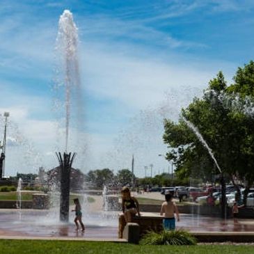 Children playing in a splash pad with fountains on a sunny day.
