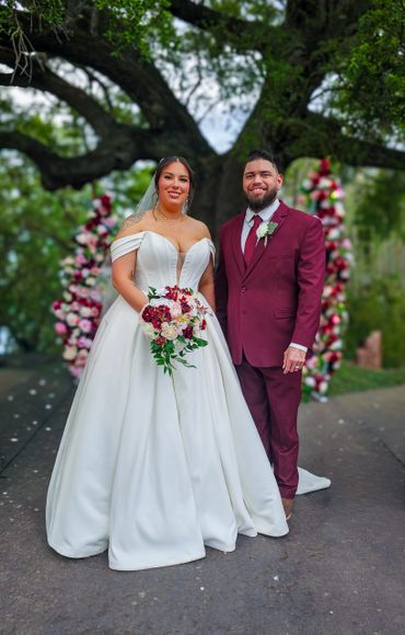 Newlywed couple posing under a large tree with floral decorations.