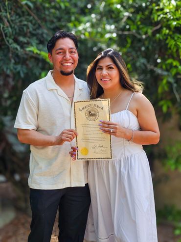 Happy couple proudly holding their marriage license outdoors.