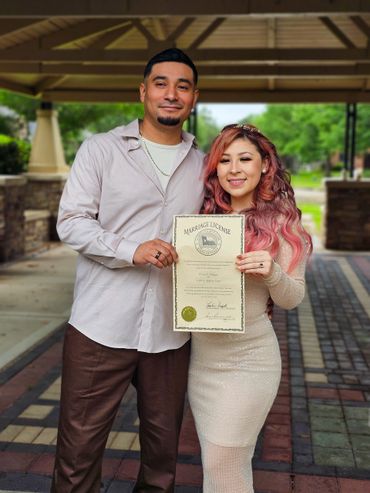 Couple proudly holding their marriage license outdoors.