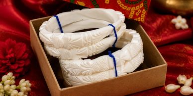 Intricately carved white bangles in a festive box.
