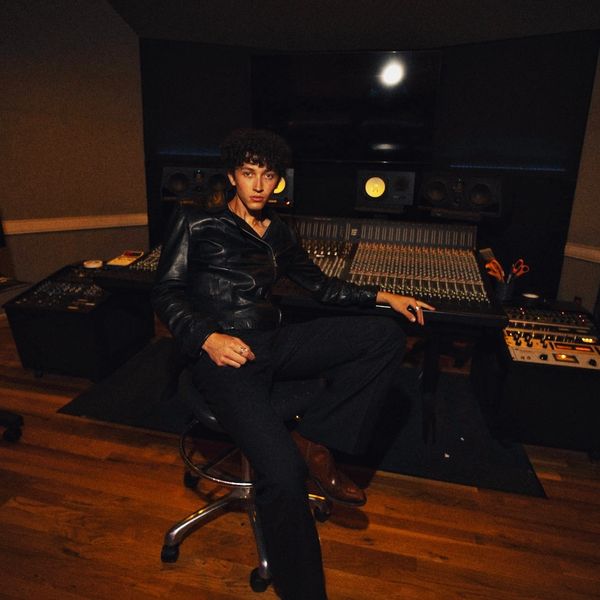 Young man in black leather jacket sitting confidently in a music studio.