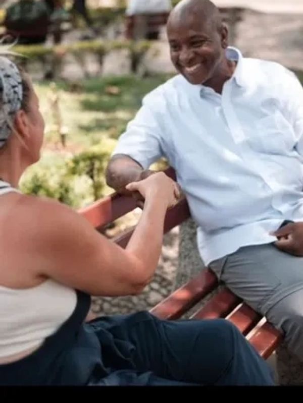 Coach shaking hands with a woman while sitting on a bench in the park.