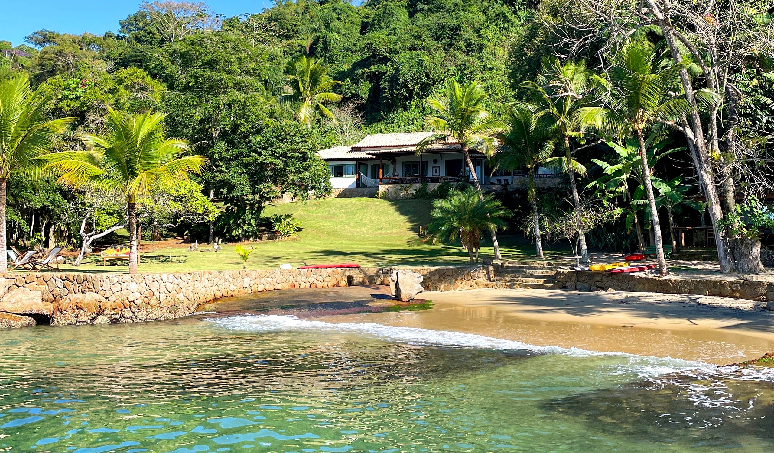 Beach house surrounded by palm trees and greenery near water.