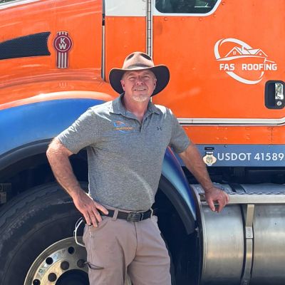 Man in hat stands by orange truck with roofing company logo.