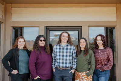 Group of five women smiling together outdoors.