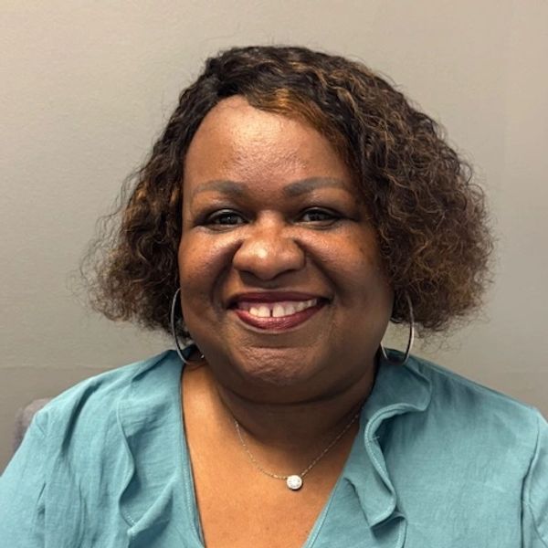 Smiling woman with curly hair wearing a teal blouse and hoop earrings.