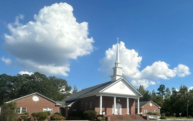 A brick church with a tall steeple under a blue sky with fluffy clouds.